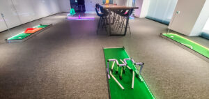 Portable mini golf course setup indoors with vibrant lighting, featuring multiple putting greens and obstacles, ideal for team-building events by Chicago Mini Golf Rentals.