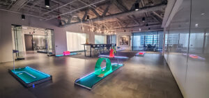 Portable mini golf course set up in a modern office space, featuring colorful illuminated holes and obstacles, emphasizing team-building activities by Chicago Mini Golf Rentals.